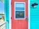 Close-up of a coral door with transom window and a digital lock, set in turquoise siding with light fixture at 308 2Nd St N # 202, Bradenton Beach, FL 34217