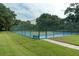 A bright blue tennis court is enclosed by a green fence and surrounded by green grass and trees at 102 Brent Cir, Oldsmar, FL 34677