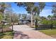 Exterior view of the property featuring a front gravel driveway, secure fence, and lush surrounding trees at 3087 Duane Ave, Oldsmar, FL 34677