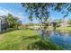 Picturesque pond view with lush green lawn, mature trees, and reflections of the sky and nearby homes at 27045 Firebush Dr, Wesley Chapel, FL 33544