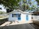 Charming white cottage with blue doors and shutters surrounded by lush trees at 14124 Plum Ln, Hudson, FL 34667