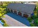 Aerial view of garage with stone exterior, gray shingle roof, 4 wood doors, pea gravel drive, and lush landscaping at 3005 S Miller Rd, Valrico, FL 33596