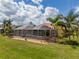 An aerial view showcasing the home with a screened-in pool, surrounded by a lush lawn and mature palm trees at 16206 Diamond Bay Dr, Wimauma, FL 33598