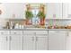 Kitchen sink boasts white cabinets, mosaic backsplash and a window with plants at 6446 Lake Sunrise Dr, Apollo Beach, FL 33572