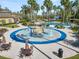 A ground view of a splash pad area with tables, chairs, and sprayers surrounded by lush landscaping at 4446 Wildstar Cir, Wesley Chapel, FL 33544
