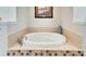 Close-up of soaking tub with brown and white tiled base, recessed lighting, and wall art at 16135 Cape Coral Dr, Wimauma, FL 33598