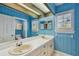 Bright, blue bathroom featuring dual sinks, a large mirror and wood paneled walls at 2508 W Shell Point Rd, Tampa, FL 33611