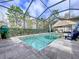 View of an in-ground pool with dark brick patio and a screened enclosure; trees can be seen beyond the enclosure at 2385 Arboretum Dr, Palm Harbor, FL 34683