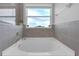Bright bathroom with a large soaking tub under a window, modern gray tile, and chrome fixtures at 10944 Delta Huff Ct, San Antonio, FL 33576