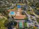 Community aerial view showcasing a pool, clubhouse, tennis courts, and shuffleboard courts surrounded by lush greenery and a pond at 2731 Sherbrooke Ln # D, Palm Harbor, FL 34684