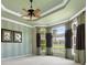 This bedroom features tray ceilings, a ceiling fan, and large windows with decorative curtains at 5062 Stone Harbor Cir, Wimauma, FL 33598