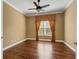 This bedroom features hardwood floors, neutral walls, a ceiling fan and a window with decorative curtains at 5062 Stone Harbor Cir, Wimauma, FL 33598