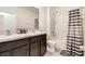 Bathroom with dual sinks, dark wood cabinets, bathtub, and shower with neutral striped curtain at 16126 Sunday Stroll Way, Odessa, FL 33556