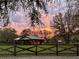 A horse barn and metal outbuilding are framed by bare tree branches and a wooden fence at dusk, creating a rustic scene at 10946 Gun Dog Way, Lithia, FL 33547