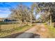 Long driveway leading to blue home and horse property, framed by mossy trees and a wooden gate, enhancing privacy at 10946 Gun Dog Way, Lithia, FL 33547