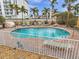 This community pool features lounge chairs, tropical foliage, and a fenced area at 11555 Gulf Blvd Blvd # 115, Treasure Island, FL 33706