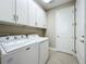 Functional laundry room equipped with a white washer and dryer, white cabinets and white door at 15434 Santa Pola Dr, Wimauma, FL 33598