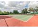 Outdoor tennis court with green and red surface, surrounded by a chainlink fence and mature shade trees at 4735 Foxshire Cir, Tampa, FL 33624