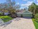 Charming green home featuring a brick-paved driveway, lush lawn, mature trees, and a well-manicured landscape at 1514 River Ct, Tarpon Springs, FL 34689