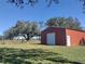 Exterior view of a sturdy storage building with a roll-up door, set on a spacious, well-maintained lawn at 8946 Old Pasco Rd, Wesley Chapel, FL 33544