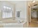 Bathroom boasts a corner tub, window with curtains, and entrance to a room with wood floors at 10416 Moshie Ln, San Antonio, FL 33576