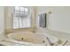 Close up view of a corner bathtub under a window featuring lace curtains, tile floors, and neutral walls at 10416 Moshie Ln, San Antonio, FL 33576