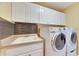 This laundry room has tile backsplash, sink, white cabinets, and front loading washer and dryer at 1335 Jumana Loop, Apollo Beach, FL 33572