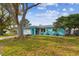 Charming blue home with mature trees in the front, a metal roof, and an orange front door at 1468 Plateau Rd, Clearwater, FL 33755