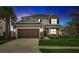 Charming two-story home at twilight featuring a well-manicured lawn, a two-car garage, and beautiful landscaping at 34159 Astoria Cir, Wesley Chapel, FL 33545