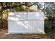 A white storage shed with a gray tin roof surrounded by grass and trees at 8436 Cameo St, Spring Hill, FL 34608
