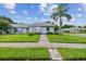 Inviting single-story home featuring a lush green lawn, manicured landscaping, and a welcoming walkway at 211 Somerset Cirle N, Dunedin, FL 34698