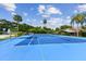 Bright blue tennis court with white lines, surrounded by lush greenery and palm trees at 211 Somerset Cirle N, Dunedin, FL 34698