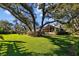 Sprawling backyard with large trees shading the lawn and a partial view of the home at 632 Royal Dornock Ct, Tarpon Springs, FL 34688