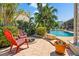 Lush backyard with palm trees, a pool, and a cozy seating area with fire pit and colorful Adirondack chairs at 725 Monte Cristo Blvd, Tierra Verde, FL 33715