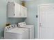 Well-lit laundry room featuring white washer, dryer, storage cabinets, and a white door at 725 Monte Cristo Blvd, Tierra Verde, FL 33715
