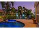 Relaxing outdoor retreat featuring a pool, spa, lounge chair and tropical landscaping under a colorful evening sky at 725 Monte Cristo Blvd, Tierra Verde, FL 33715