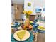 Close-up of a dining table set with blue glassware and green napkins with a peek of the living room at 8901 Blind Pass Rd # 224, St Pete Beach, FL 33706