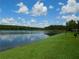 Picturesque lake view with clear water and a grassy shoreline, under a bright sky at 18106 Peregrines Perch Pl # 5208, Lutz, FL 33558