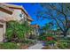 Beige stucco home with red tile roof, blue shutters, manicured front yard with trees, and a clear blue sky at 4677 Aylesford Dr, Palm Harbor, FL 34685