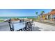 Outdoor dining area overlooking the beach, with a white table and striped chairs, perfect for enjoying ocean views at 2411 And 2407 Casey Key Rd, Nokomis, FL 34275
