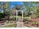 An inviting backyard showcases a white arbor entrance, brick pathway, and lush landscaping, creating a welcoming outdoor space at 2823 Clubhouse Dr, Plant City, FL 33566