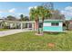 Inviting home with a well-manicured lawn, mature palm trees, a carport, and bright orange doors at 1868 Douglas Ave, Dunedin, FL 34698