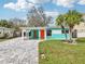 Inviting home with a well-manicured lawn, mature palm trees, a carport, and bright orange doors at 1868 Douglas Ave, Dunedin, FL 34698