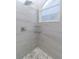 Close-up of a glass shower with tile walls, pebble floor, glass corner shelves, and a window at 9376 French Quarters Cir, Weeki Wachee, FL 34613