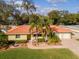 Charming one-story home with a bright orange tile roof, brick driveway, and lush tropical landscaping at 220 Garden S Cir, Dunedin, FL 34698