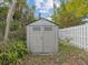 Gray storage shed with double doors, small windows, and a gable roof surrounded by greenery and a white picket fence at 605 Gardenia St, Belleair, FL 33756