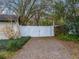 Gated driveway entrance featuring white privacy gates, mature landscaping, and gravel driveway at 503 Hillpine Way, Brandon, FL 33510