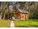 Quaint wooden cabin surrounded by lush trees, featuring a covered porch and stone pathway at 13381 Glory Ln, Brooksville, FL 34614