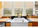 Close up of a white farmhouse kitchen sink beneath three windows overlooking a green and lush outdoor area at 13381 Glory Ln, Brooksville, FL 34614