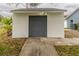 Exterior view of the one-car detached garage with white facade and gray door near a swimming pool area at 17508 Isbell Ln, Odessa, FL 33556